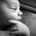 A baby with a hand on their chin looking thoughtful in a black and white photograph.