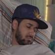 Man wearing a blue baseball cap sleeping on a pillow.