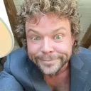 Man with curly hair making a wide-eyed, mischievous facial expression.