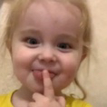 Toddler holding a finger to their lips with a mischievous smile.