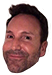 Man with short dark hair and stubble wearing a smug, knowing grin.
