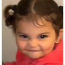 Toddler with pigtails making a mischievous, knowing smirk at the camera.
