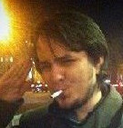 Man saluting with a cigarette in his mouth in a dimly lit setting.