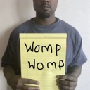 Kanye West holding a yellow notepad with the words Womp Womp written in black marker.