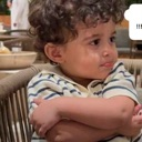 A toddler with curly hair looking sideways with a skeptical expression and arms crossed.