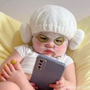 A baby wearing a white spa headband and gold eye patches looking intensely at a smartphone.