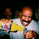 Steve Harvey laughing hysterically while pouring a yellow drink into a glass.