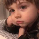 A young child resting their chin on their hand with a bored and unimpressed facial expression.
