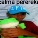 A person wearing a blue baseball cap holds a green plush frog toy in a low-resolution selfie.