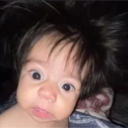 Baby with wide eyes and messy hair looking shocked and confused.