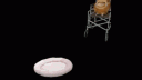 A brown cat sitting in a wheelchair before hopping out onto a small pink pet bed.