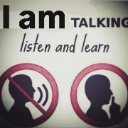 A sign featuring two silhouettes, one speaking and one shushing, with the text I am talking listen and learn.