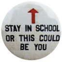 A circular white badge with black text reading Stay In School Or This Could Be You and a red arrow pointing upwards.