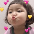 A toddler with a bob haircut blowing a kiss surrounded by pink and yellow heart icons.