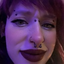 A goth woman with multiple facial piercings looking at the camera with a confused and skeptical expression under purple li...