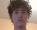 Young man with curly hair looking directly at the camera with a neutral, unimpressed expression.