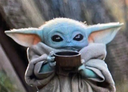 A small green alien with large eyes holding a cup and sipping from it.