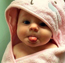 Baby wrapped in a pink hooded towel sticking its tongue out playfully.