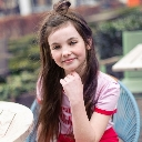 Young girl with brown hair resting her chin on her hand while smiling gently.