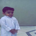 A young boy in a white thobe looking at the camera with a skeptical and unimpressed expression.