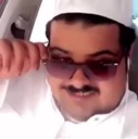 Man wearing a white kufi and thobe adjusting his purple-tinted sunglasses with a smug, confident smile.