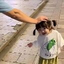 A toddler with pigtails smiles while receiving a gentle pat on the head from an adult.