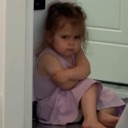 Toddler sitting on the floor with arms crossed and a stern, grumpy facial expression.