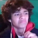 Young man with curly hair and headphones making a confused and vacant facial expression.