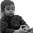 A young child with a serious expression looking down while holding their hands together.