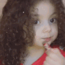 A young girl with curly hair applying red lipstick to her lips.