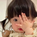 A young child with dark hair covers one eye with their hand while looking at the camera.