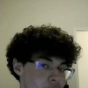 Young man with curly hair and glasses staring intensely with a suspicious expression.