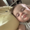 Baby sleeping peacefully with eyes closed on a yellow pillow.
