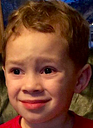 A young child with brown hair wearing a red shirt gives a forced, uncomfortable side-eye smile.