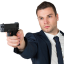 Man in a suit pointing a black handgun directly at the viewer with a serious expression.