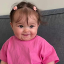 Toddler with a mischievous smirk and pink hair clips wearing a pink shirt.