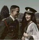 A man in a military uniform and a woman in a formal hat smiling together in a vintage-style photograph.