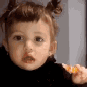 A toddler making a skeptical face while holding a piece of orange food.