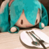 Hatsune Miku plushie bobbing its head while looking at a plate with cutlery.