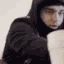Yeat wearing a hoodie while pouring liquid into a white styrofoam cup.