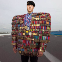 A person stands wearing a jacket completely covered in dozens of military medals, creating an exaggerated, wide-shouldered s…