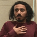 A man with wide eyes looking shocked while holding his hand over his chest.