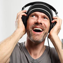 Man wearing a beanie and headphones looking up with a wide, excited expression.