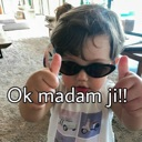 A young child wearing dark sunglasses gives a double thumbs-up gesture with the text Ok madam ji!! overlaid.
