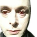 A pale face with glowing red eyes stares directly forward with an intense, unsettling expression.