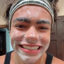 A person with a white face mask and a headband smiling broadly at the camera.