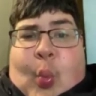 A person with glasses making a distorted, exaggerated pucker face.