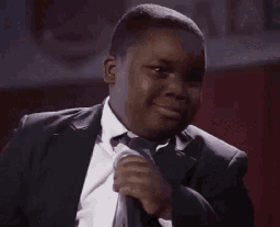 A young boy in a suit slowly turns his head and gives a smug, knowing smirk.