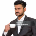 Businessman in a suit holding a white coffee cup and looking away with a serious expression.