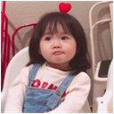 A toddler with a deadpan expression wears a small red heart on their head.